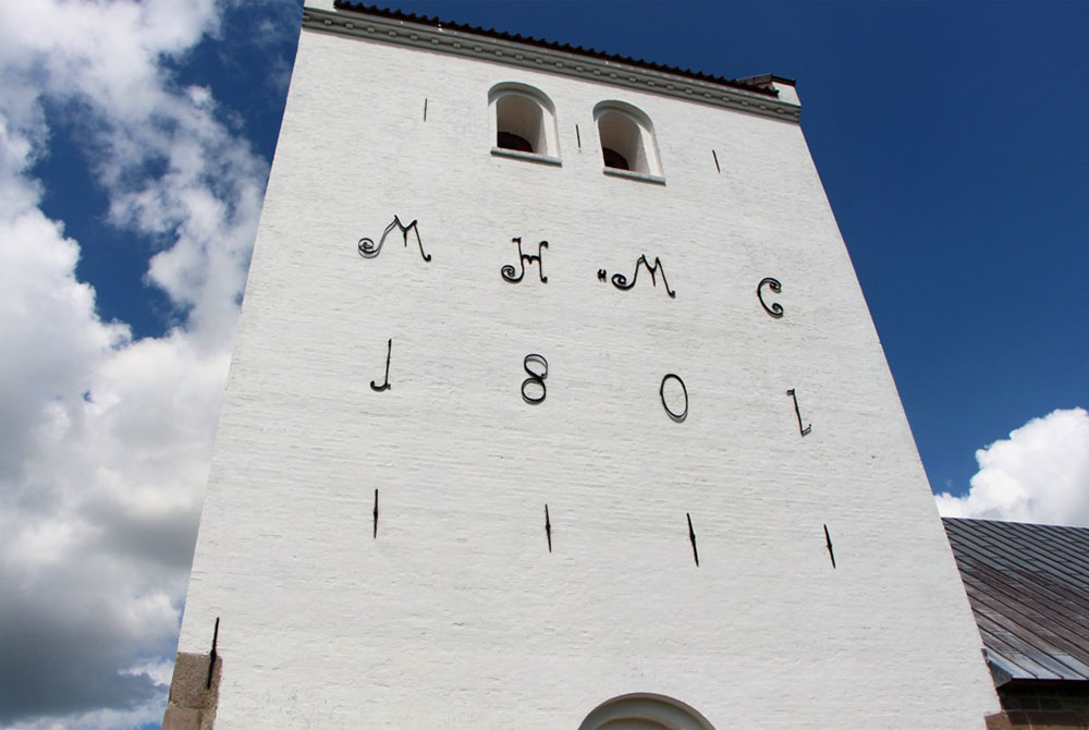 Kettrup Kirkes monumentale tårn, der rummer hele to klokker og udvendig bærer initialerne på en af godsejerne fra Aagaard, Mathias Hviid samt hustru, Mariane Colding. Foto: Bjarne Bjerregaard Jørgensen.