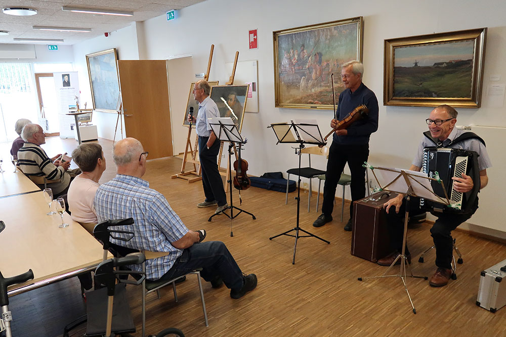 Niels Kraghede (th) sammen med sin trio – Niels Kraghede på harmonika samt Erik Nordholt og Johan Svaneborg på violin – her ved ferniseringen på kunstudstillingen om Svinkløvmalerne i Fjerritslev Kirkecenter i juni 2019